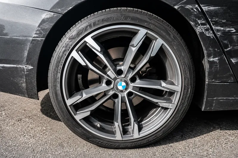 Kratzer und Schrammen an Radlauf und Seitenteil eines dunkelgrauen BMW neben der Alufelge
